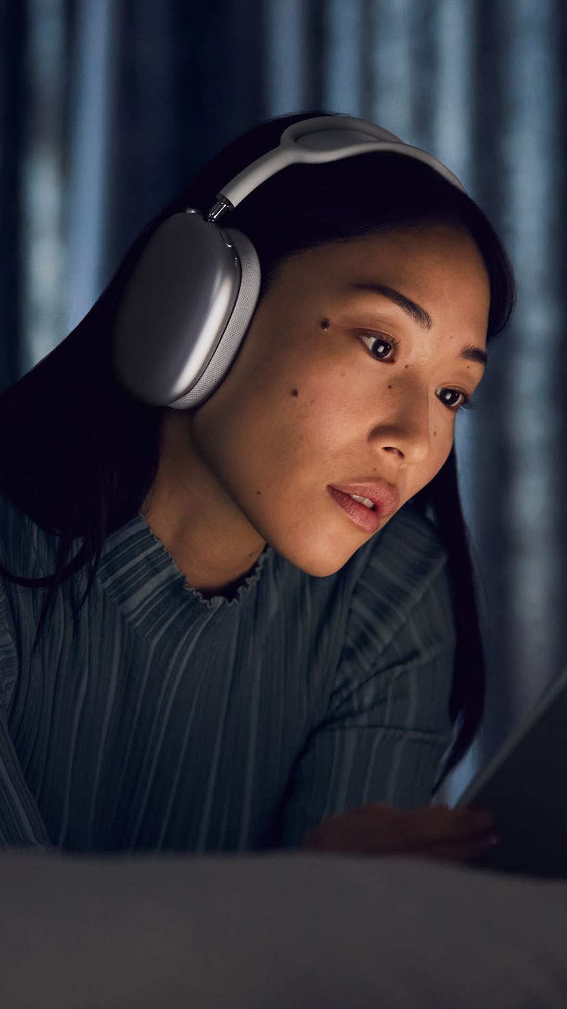 A woman wears Apple's new AirPods Max while on her iPad at night.