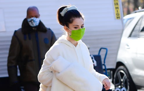 Selena Gomez in a cream tracksuit and black Ugg boots, with a lime face mask, carrying a cream plush...