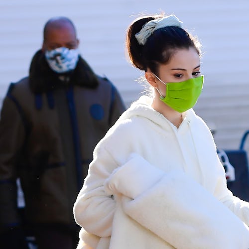 Selena Gomez in a cream tracksuit and black Ugg boots, with a lime face mask, carrying a cream plush...
