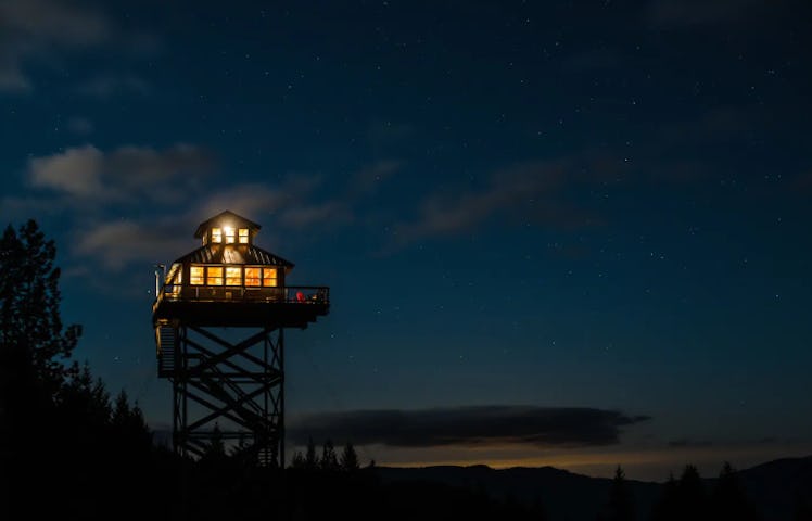 A tower listed on Airbnb sits above the trees in Oregon, all lit up in the evening.