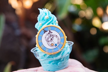 A woman holds up a blue, sparkly Cinderella Dole Whip with a white chocolate clock at Disney. 
