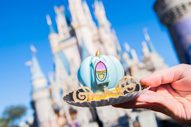 A woman holds up a 'Cinderella' treat made to look like her carriage in front of the castle at Disne...