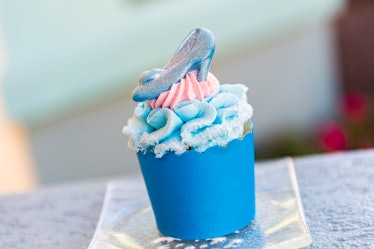 A blue and pink 'Cinderella'-inspired cupcake sits on the table with a chocolate glass slipper on to...