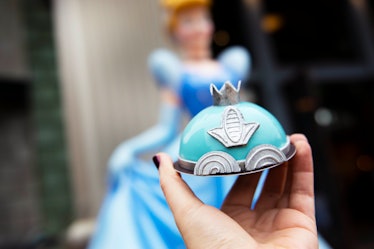 A woman holds up the Cinderella Mini Dome Cake that's available at Disney Springs, in front of a Cin...