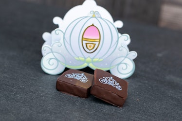 Two pieces of chocolate sit on the table in front of a chocolate box that's shaped like Cinderella's...