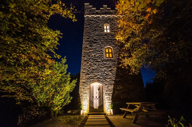 A castle tower in Ireland that is listed on Airbnb is lit up with lights at night. 