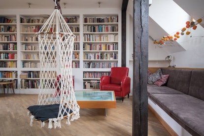 A swing hangs in the middle of a living room on Airbnb with bookshelf walls, just like the library i...
