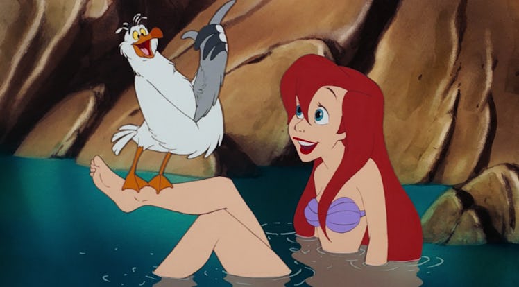 Ariel sits in the water on the beach with Scuttle in 'The Little Mermaid.'