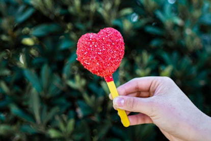 A woman holds up the Queen of Hearts inspired heart-shaped cake pop from the Disney Villains After H...