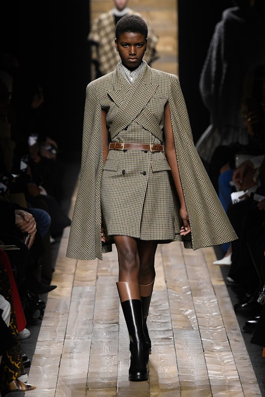The model wears a beige checkered, belted blazer dress with flared sleeves from Michael Kors 2020 Fa...