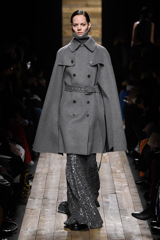 The model wears a grey midi coat with flared sleeves over glittery flared pants from Michael Kors Fa...