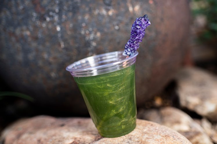 A green lemonade inspired by Dr. Facilier from 'The Princess and the Frog' sits on a rock at the Dis...