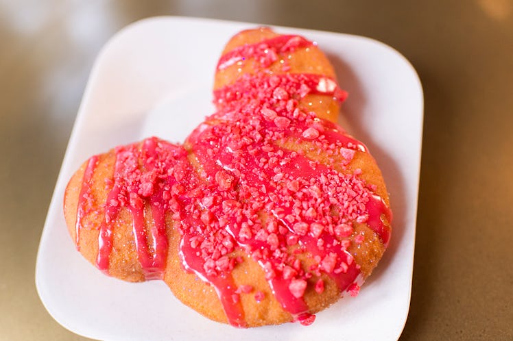 A Mickey Mouse-shaped cinnamon beignet sits on a plate with red drizzle for Valentine's Day at Disne...