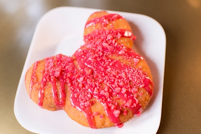 A Mickey Mouse-shaped cinnamon beignet sits on a plate with red drizzle for Valentine's Day at Disne...