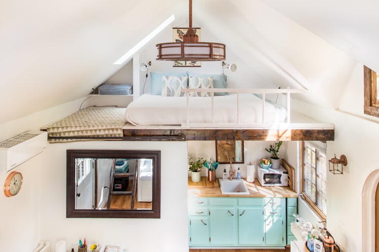 A tiny home is designed to look very cozy with teal cabinets, lots of natural sunlight, and a lofted...