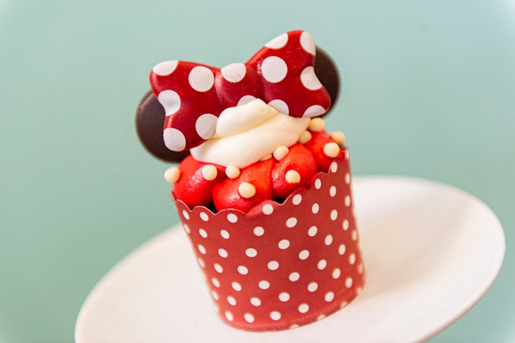 A Minnie Mouse cupcake with chocolate ears and red and white icing sits on the table for Valentine's...