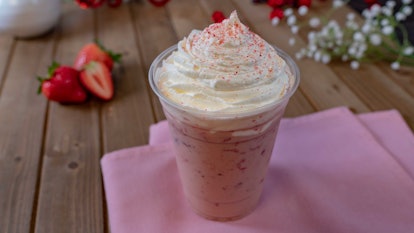 A pink Strawberry Horchata has whipped cream and a strawberry on top, while sitting on a table durin...