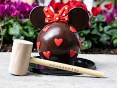 A Minnie Mouse-shaped chocolate piñata sits on the table with a wooden mallet for Valentine's Day at...