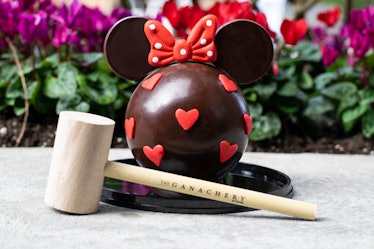 A Minnie Mouse-shaped chocolate piñata sits on the table with a wooden mallet for Valentine's Day at...