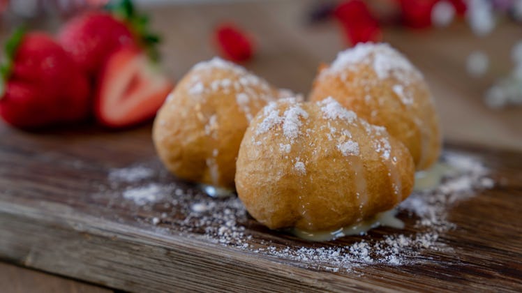Three berry cheesecake fritters are topped with powder sugar on a wooden table.
