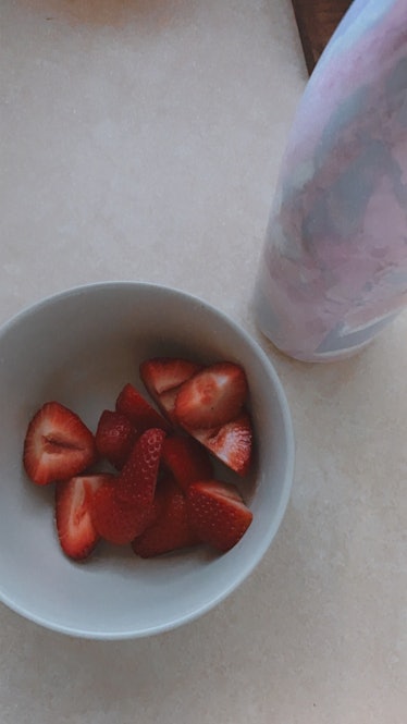 A bowl of strawberries sits next to a colorful water bottle on a kitchen counter.
