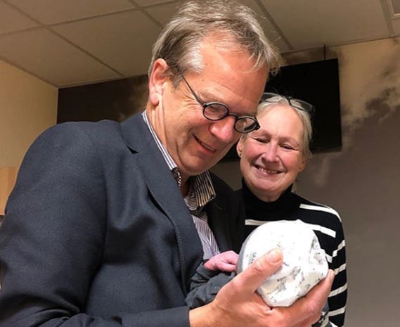 A man and woman, first-time grandparents, smile down at their newborn grandchild.