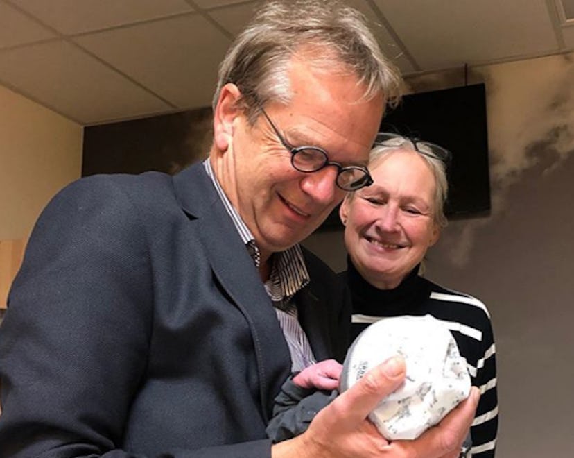 A man and woman, first-time grandparents, smile down at their newborn grandchild.