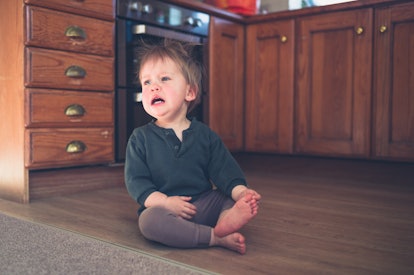 Toddler throws head back during tantrum while sitting on the kitchen floor at home
