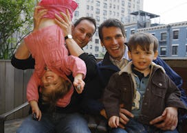 Two dads play with their kids, one dangled upsidedown