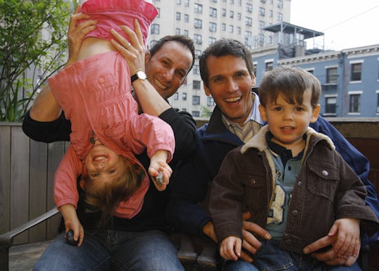 Two dads play with their kids, one dangled upsidedown