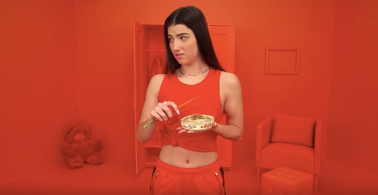 Charli D'Amelio's wears a red top and pants while holding a tub of hummus in Sabra Hummus' 2020 Supe...