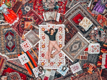 A woman lounges on a bunch of colorful rugs at a rug store in Cappadocia, Turkey.