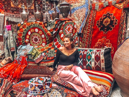 A woman poses on an assortment of colorful rugs and pillows at a rug store in Turkey. 