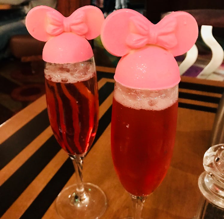 Two pink glittery mimosas with Minnie Mouse toppers are placed on a wood table at The Wave at Disney...