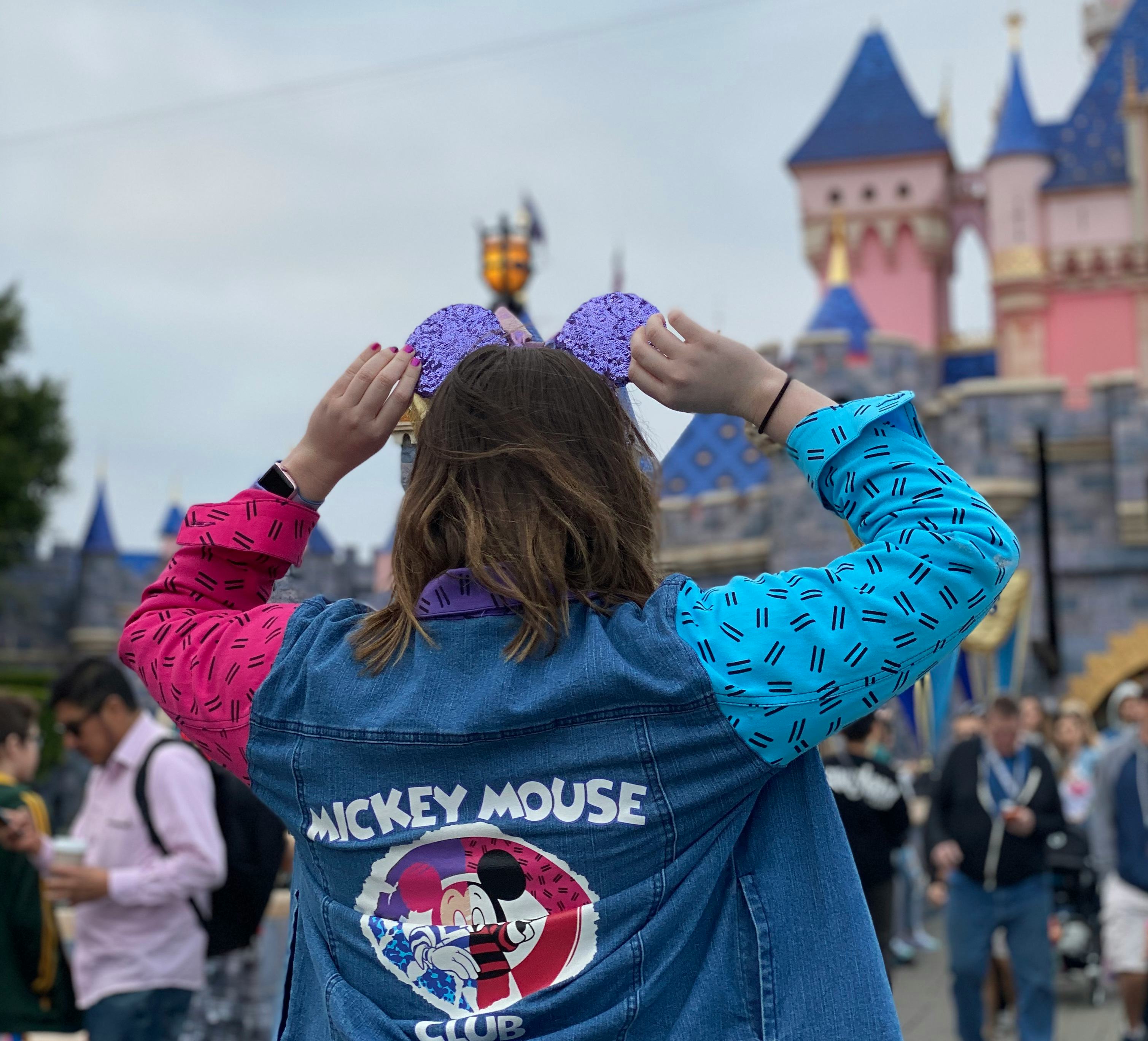 A woman holds her sparkly purple Mickey Mouse ears while standing in front of the castle at Disneyla...