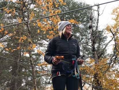 A woman dressed in a gray beanie, black jacket, and black leggings smiles on a fall day while gearin...