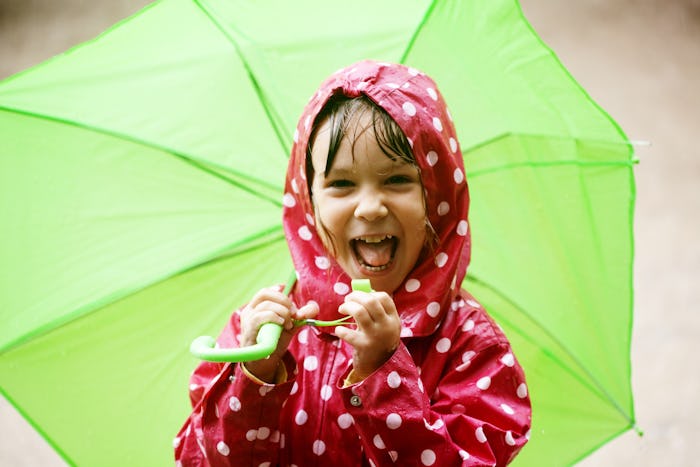 Smiling child in red raincoat with white polkadots holds a big green umbrella