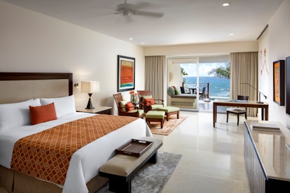 A suite at Grand Velas Riviera Maya features a comfortable bed with orange and red accents, and a ba...