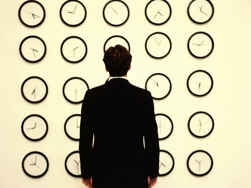 A man in a suit standing in front of a wall full of clocks