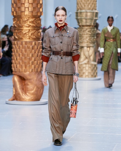 A model in a brown coat with red highlights, and a belt walks the runway at chloe's fall 2020 show