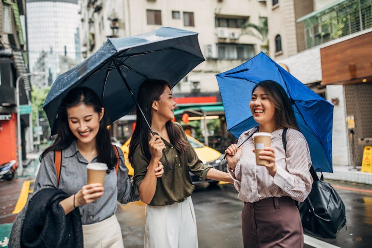 Three Asian female friends in the rain with umbrellas and coffee