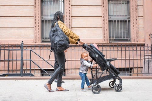 Mom pushing stroller, helped by toddler