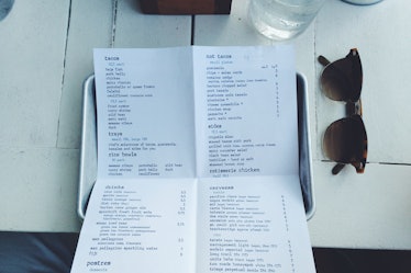 A taco menu sits open on a table next to a pair of sunglasses.