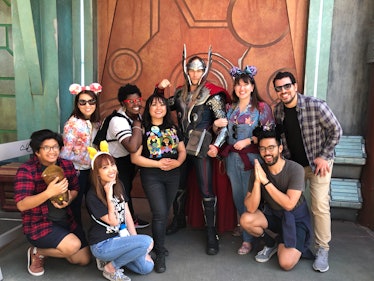 A big group of friends wearing Mickey Mouse ears pose and smile with Thor at Disneyland 