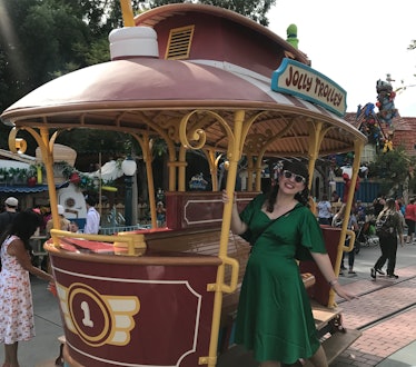 A woman in a long green dress and sunglasses smiles and poses on the trolley in Toontown at Disneyla...