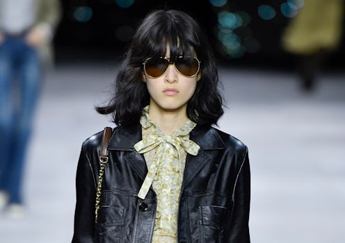 A model on a runway in a beige floral top and a black leather blazer
