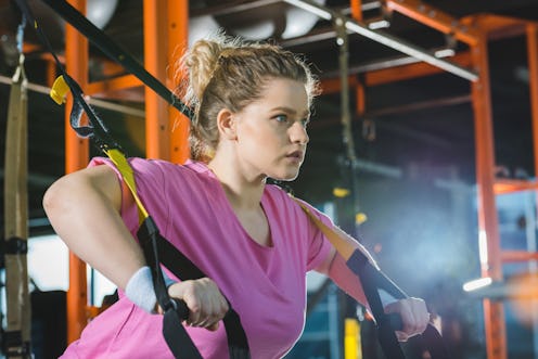 A person in a pink t-shirt and white wristbands performs a TRX pushup. Getting back to the gym after...