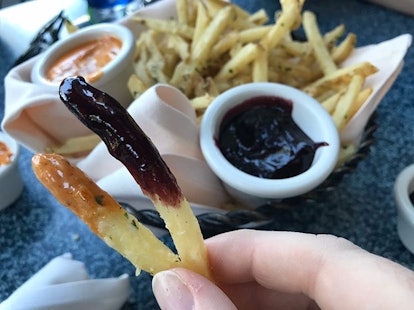A woman's hand holds up two pomme frites dipped in off the menu sauces at Disneyland. 
