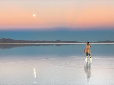 A woman dressed in white boots, earmuffs, jeans, and a warm jacket walks in a shallow body of water ...