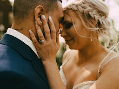 A couple embraces each other on their wedding day while dressed up and standing outside a cozy home.